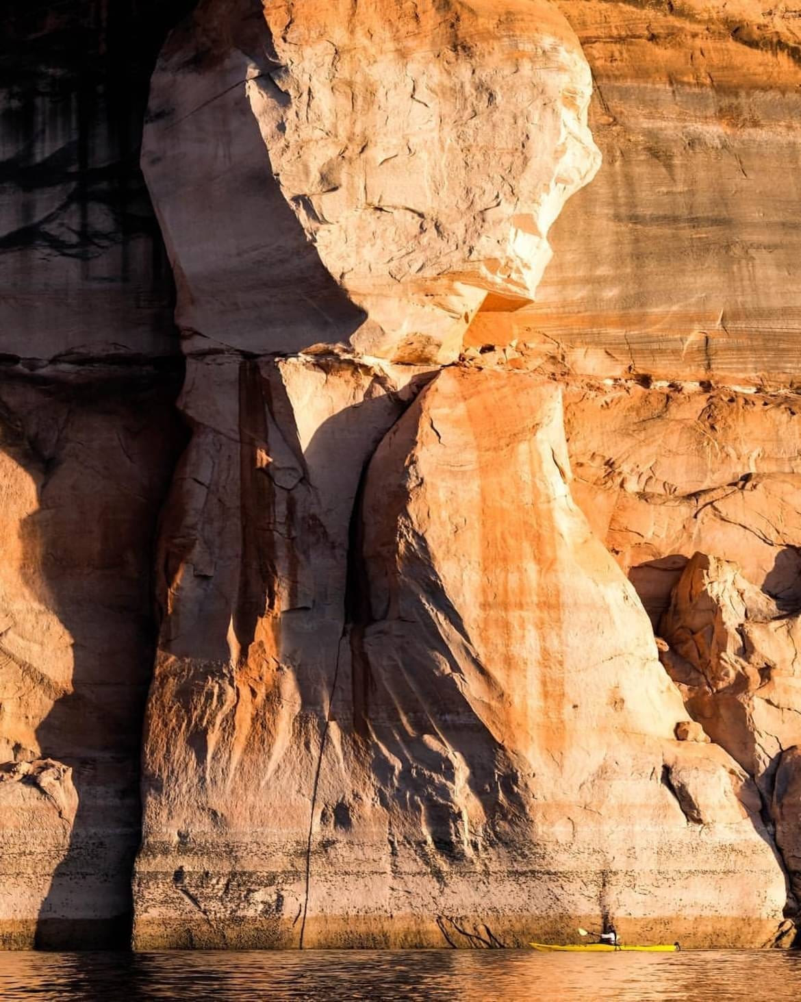 Sunlight illuminating the orange sandstone walls above a narrow stretch of water.