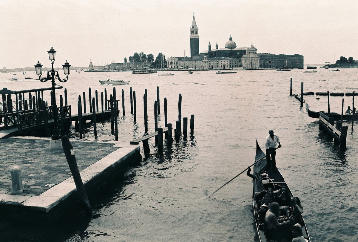 Gondolas moored along a waterfront, with a church and bell tower across the water.