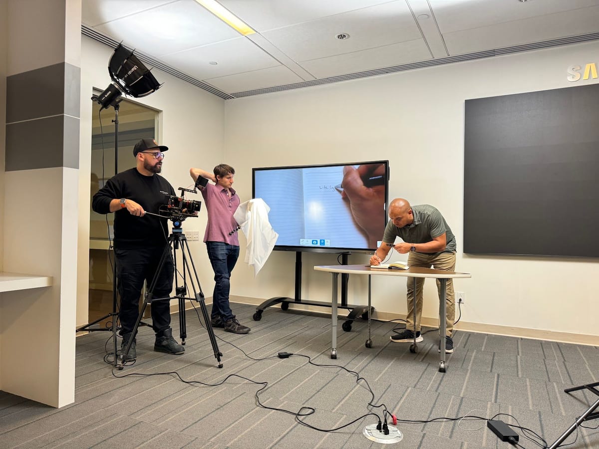 Carolyn with a camera operator and presenter on a studio set featuring an interactive display.
